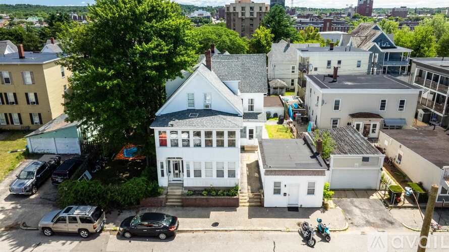 A white house with a blue roof is surrounded by other houses and cars.