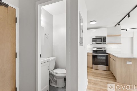 A modern kitchen with a toilet and sink visible through an open door.