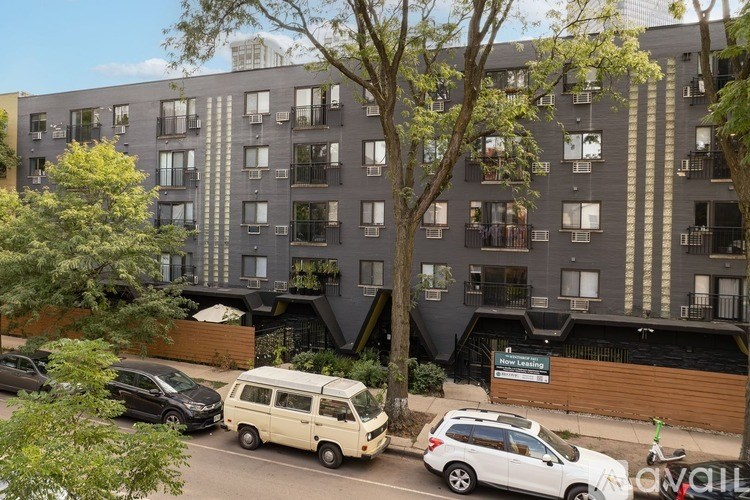 A street view of a residential area with cars parked on the side of the road and apartment buildings in the background.