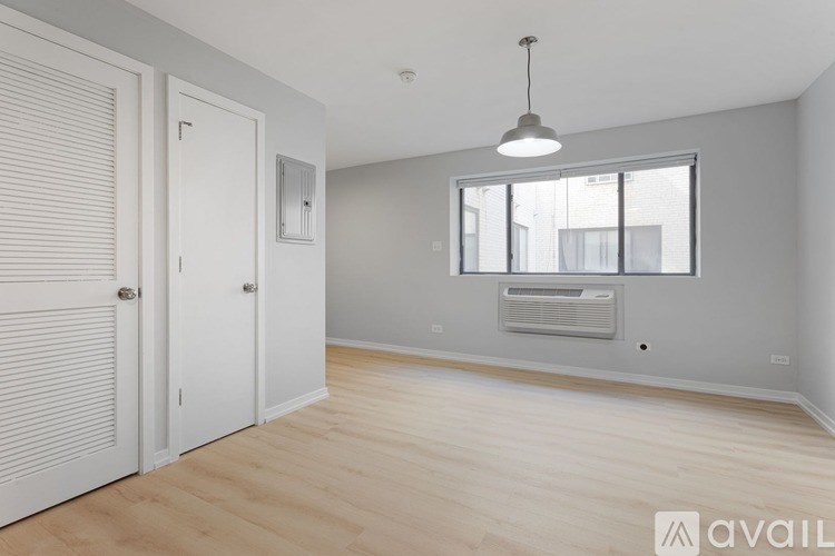 A room with a wooden floor, a window with blinds, a white door, and a hanging light fixture.