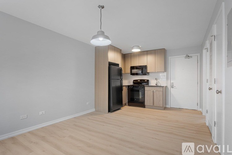 A kitchen with a black fridge and microwave, wooden floors, and white walls.