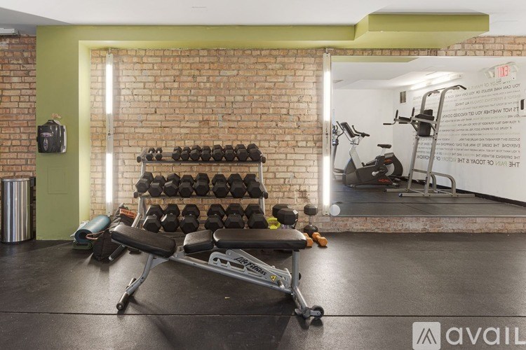 A gym with a brick wall and a variety of equipment including dumbbells, a bench, and a treadmill.