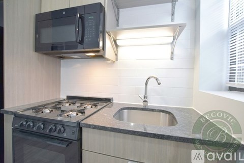 A modern kitchen with a black microwave above the stove and a stainless steel sink.
