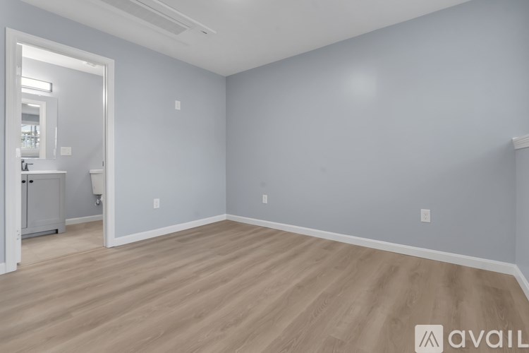 A room with light grey walls and wooden flooring with a white door leading to another room.
