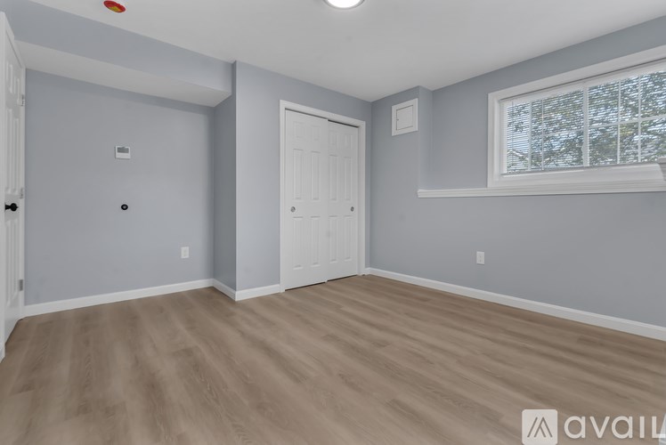 A room with a white door and a window with a view of trees outside.