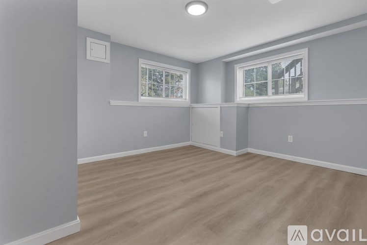 A room with light grey walls and wooden flooring with a window on the right.