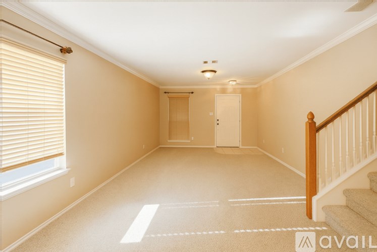 A spacious room with a staircase on the right and a window with blinds on the left.