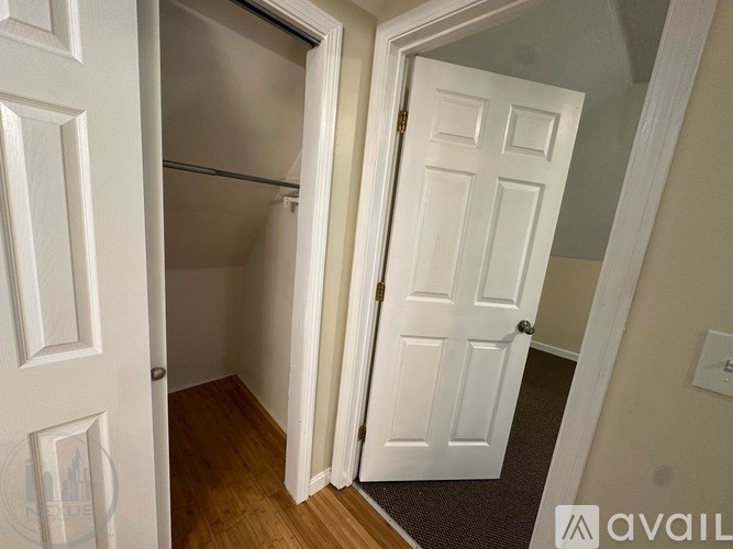 A white door is open to a small, empty room with a wooden floor.