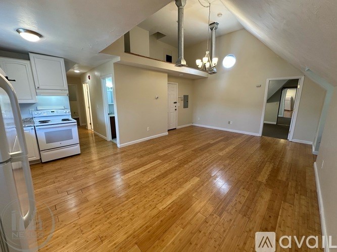 A spacious room with wooden flooring and a kitchen area with white appliances.