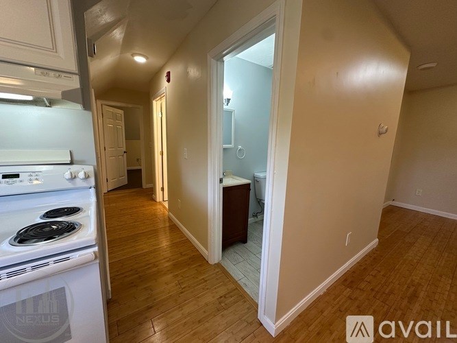 A kitchen with a stove top oven and a hallway with a doorway leading to a bathroom.