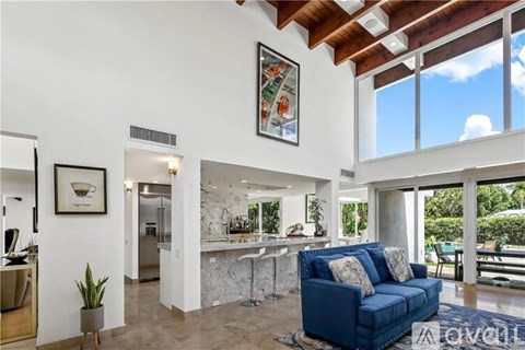 A blue couch sits in a spacious living room with a kitchen in the background.