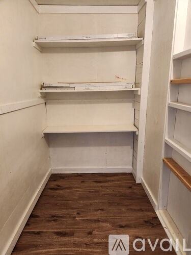 A white shelving unit with three shelves is in a room with wooden flooring.