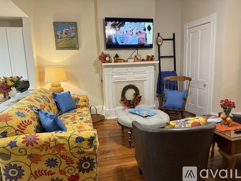 A living room with a yellow floral couch, a white fireplace, and a television mounted above it.