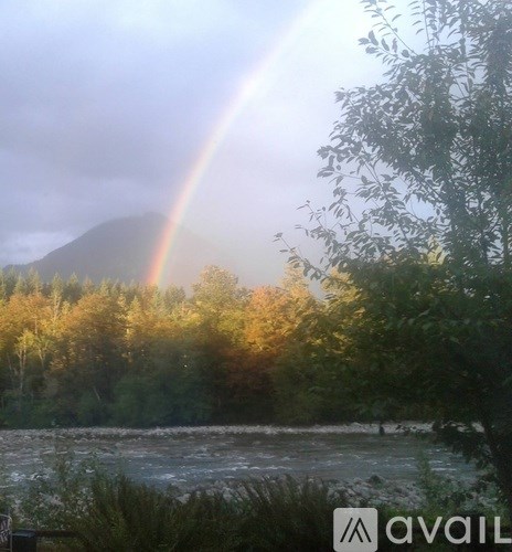 A rainbow appears over a river with trees in the background.