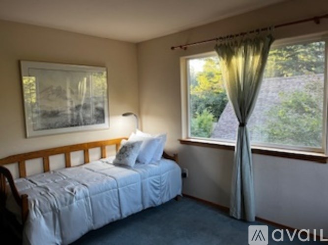 A bedroom with a bed, a window with a curtain, and a painting on the wall.