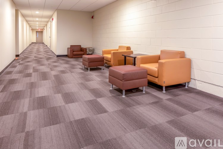 A hallway with a carpeted floor and a row of chairs on the right side.