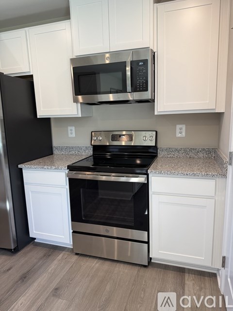 A kitchen with a black refrigerator, stainless steel oven, and white cabinets.