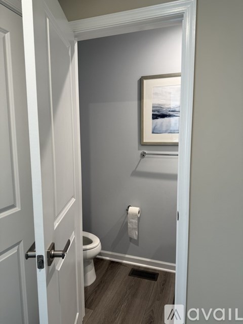 A white door is open to a small bathroom with a toilet and a picture on the wall.
