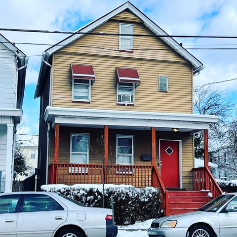 A house with a red door and a red awning is in front of a white car.