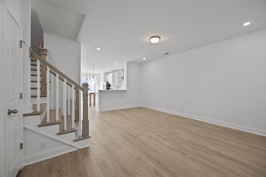 A spacious room with wooden flooring and a staircase with white railings.