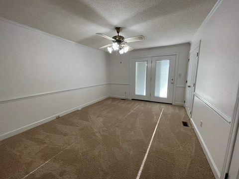 A room with a carpeted floor and a ceiling fan.