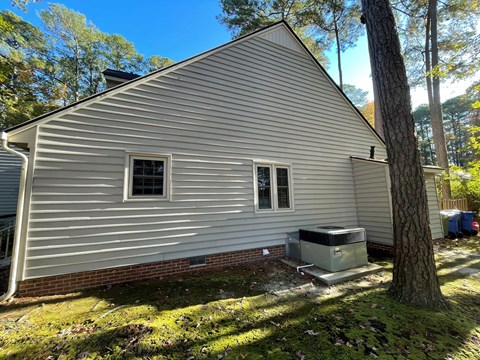 A small house with a grey siding and a brick foundation.
