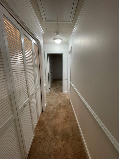 A long hallway with white walls and a brown carpet.