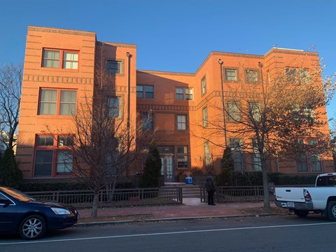 A blue car is parked on the side of the street in front of a brick building.
