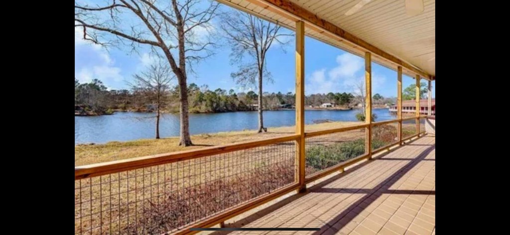 A wooden deck overlooks a lake with trees in the background.