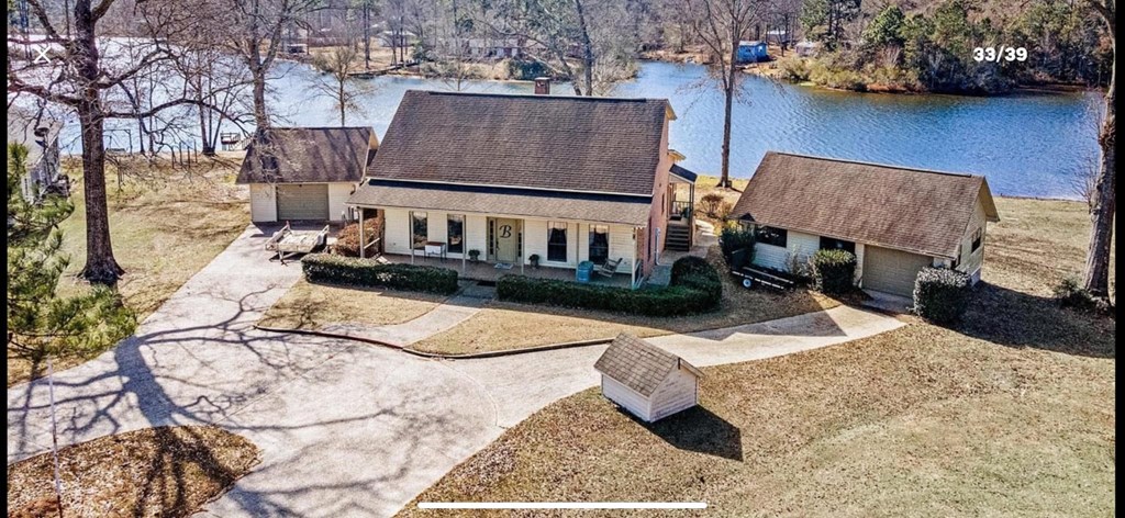 A house with a brown roof is surrounded by a grassy area and a lake.