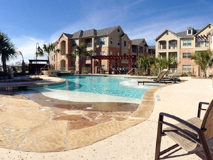 A pool surrounded by a stone patio and a building in the background.