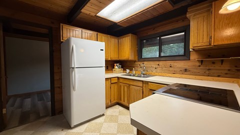 A white refrigerator stands in a kitchen with wooden cabinets and a window.