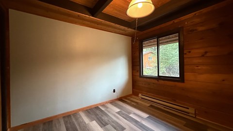 A room with wooden walls and a window showing a view of a house and trees.