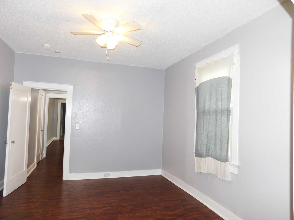 A room with a ceiling fan and a window with a curtain.