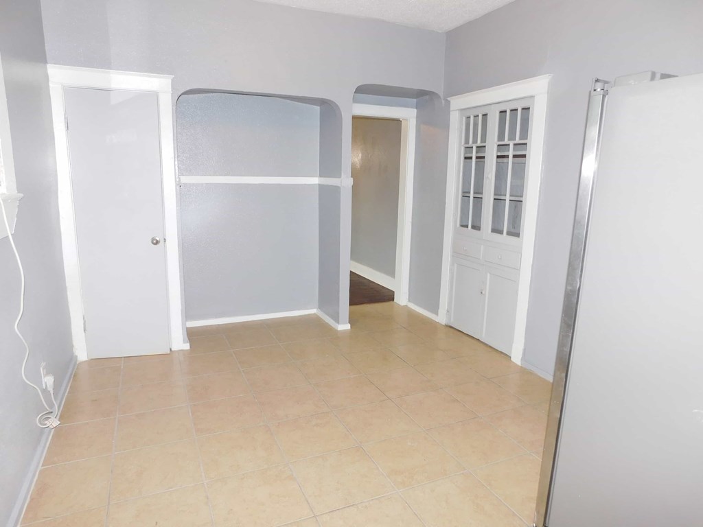 A room with a white door, a white wall, and a brown floor.