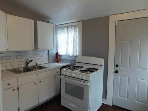 A white kitchen with a stove, sink, and cabinets.