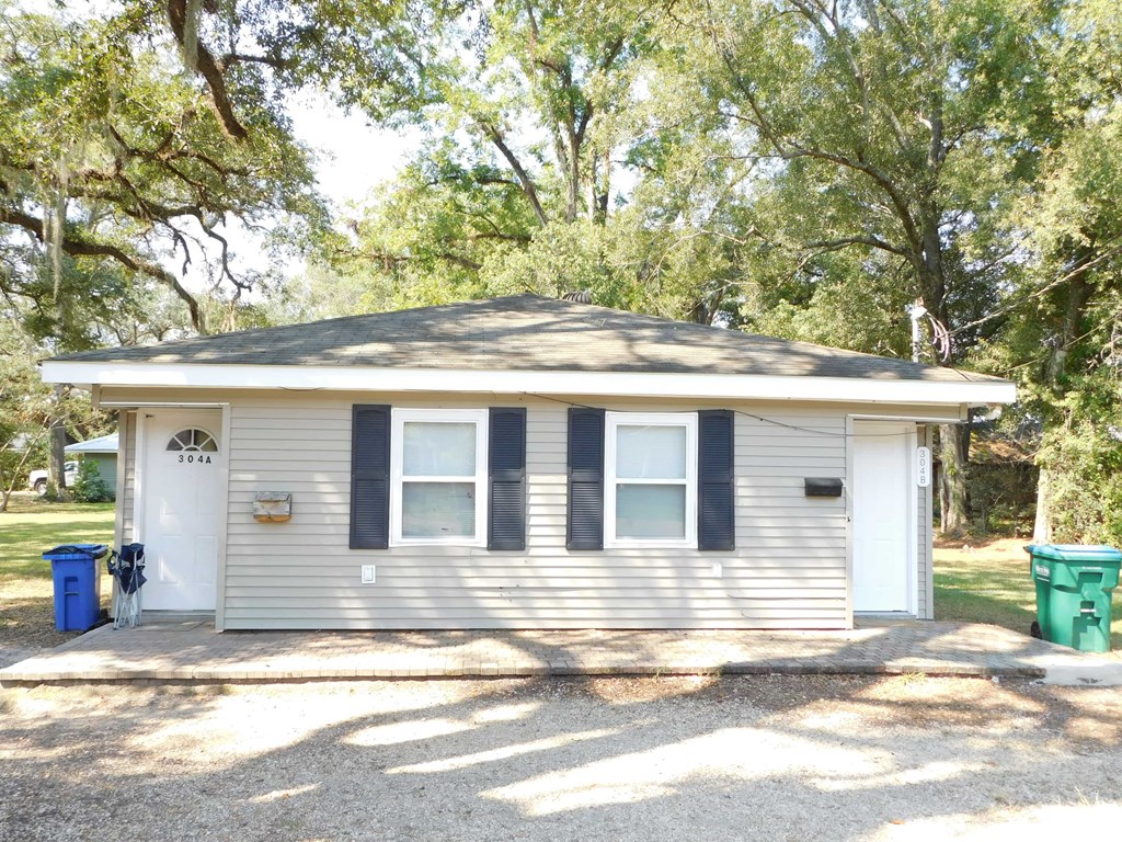 A small house with a grey roof and a white door is surrounded by trees.