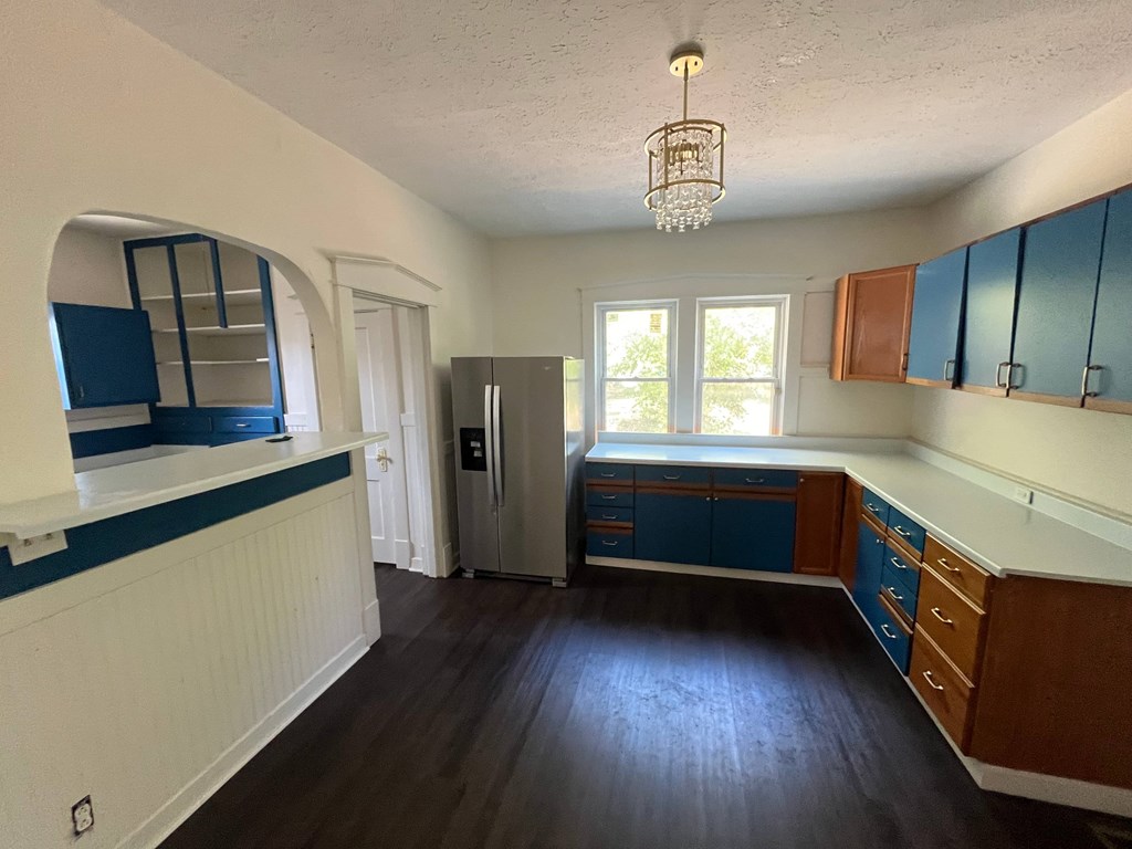 A kitchen with a refrigerator, cabinets, and a window.