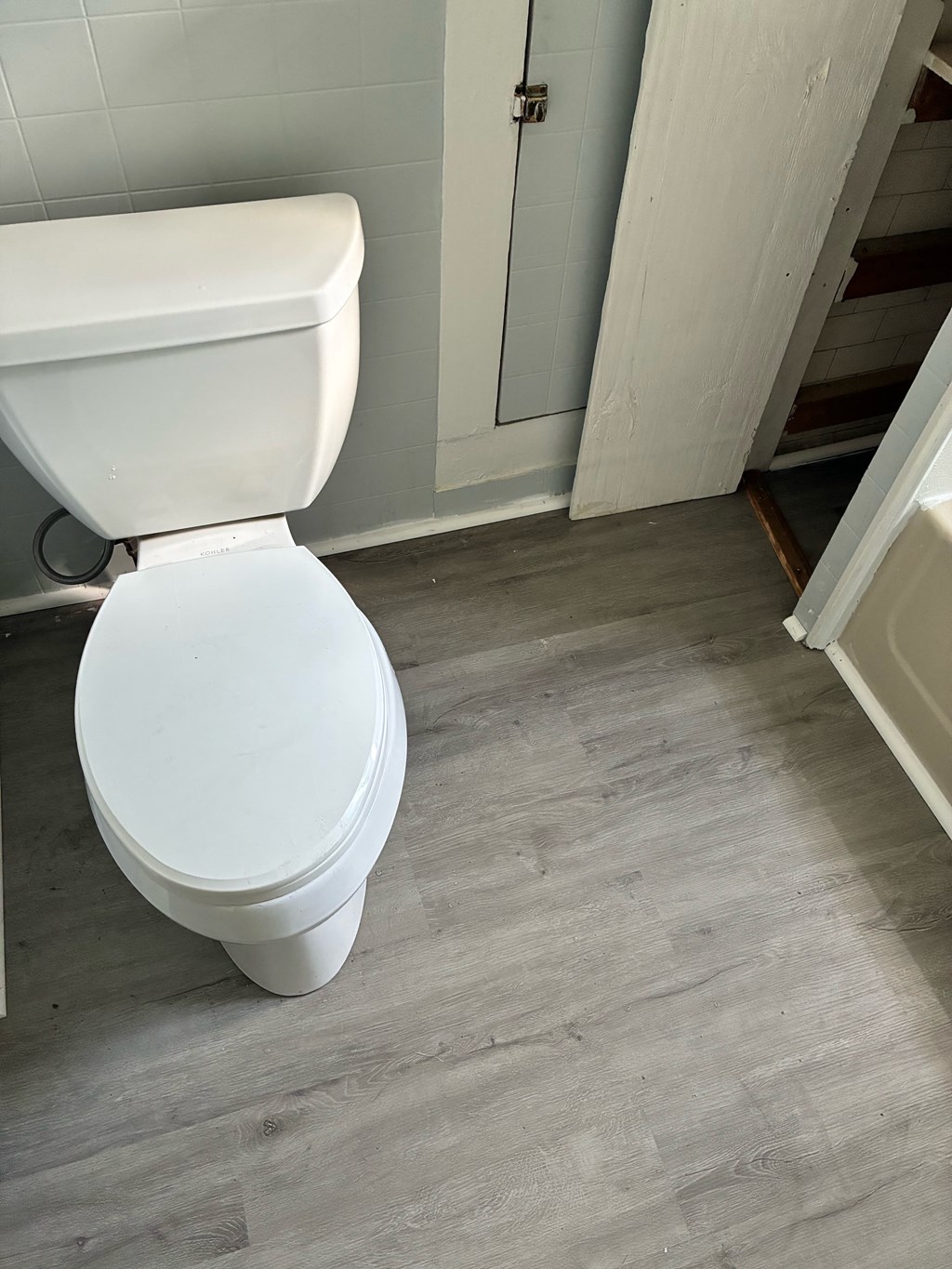 A white toilet in a bathroom with a wooden floor and a white door.
