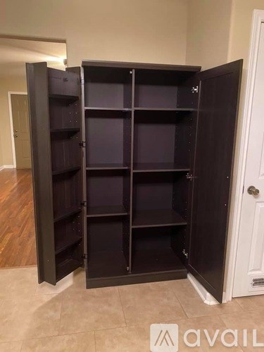 A large black wardrobe with shelves is open in a room.