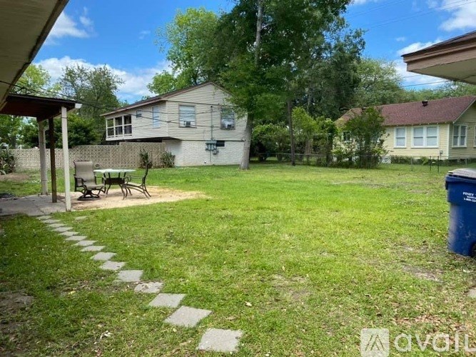 A backyard with a lawn, a trash can, and a pathway leading to a house.