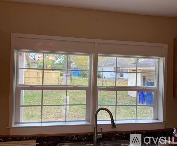 A kitchen window with a view of a backyard and a blue container.
