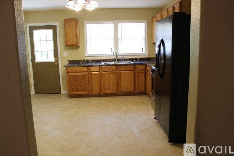 A kitchen with a black refrigerator, wooden cabinets, and a window.