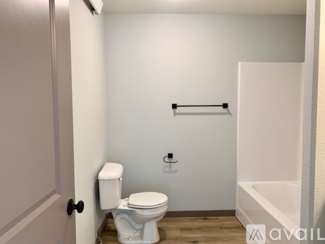 A white toilet in a small bathroom with a white door and a white bathtub.