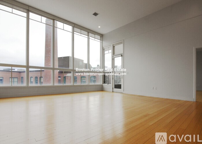 A large empty room with wooden floors and a view of a building outside the window.