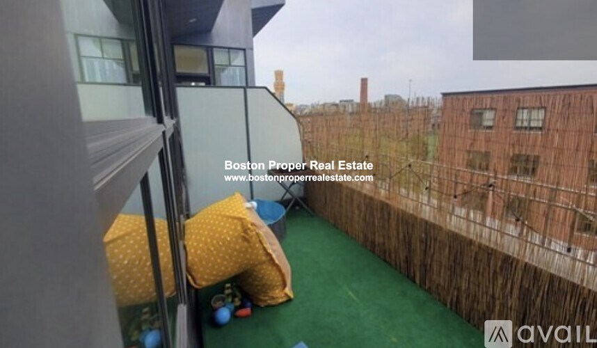 A balcony with a green carpet and a view of a brick building.