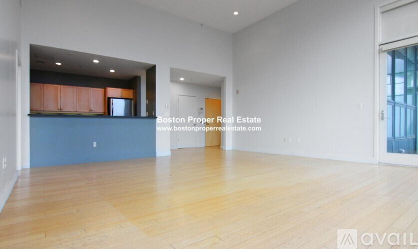 A large empty room with wooden floors and a kitchen area in the background.
