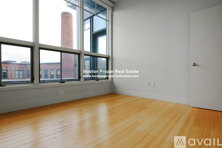 A room with wooden flooring and a view of a brick building through large windows.