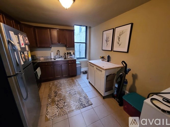 A kitchen with a refrigerator, cabinets, and a rug on the floor.