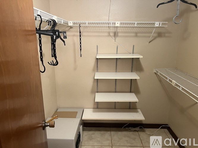 A small walk-in closet with a white shelf and a brown door.